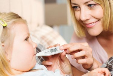 Ein Kind, das im Bett liegt, und eine Frau, die ihr mit dem Fieberthermometer im Mund misst.